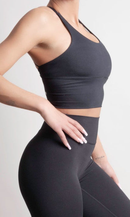 Model wearing NOIR Cross Top Black Women with leggings and sneakers, showcasing dynamic movement and comfort.