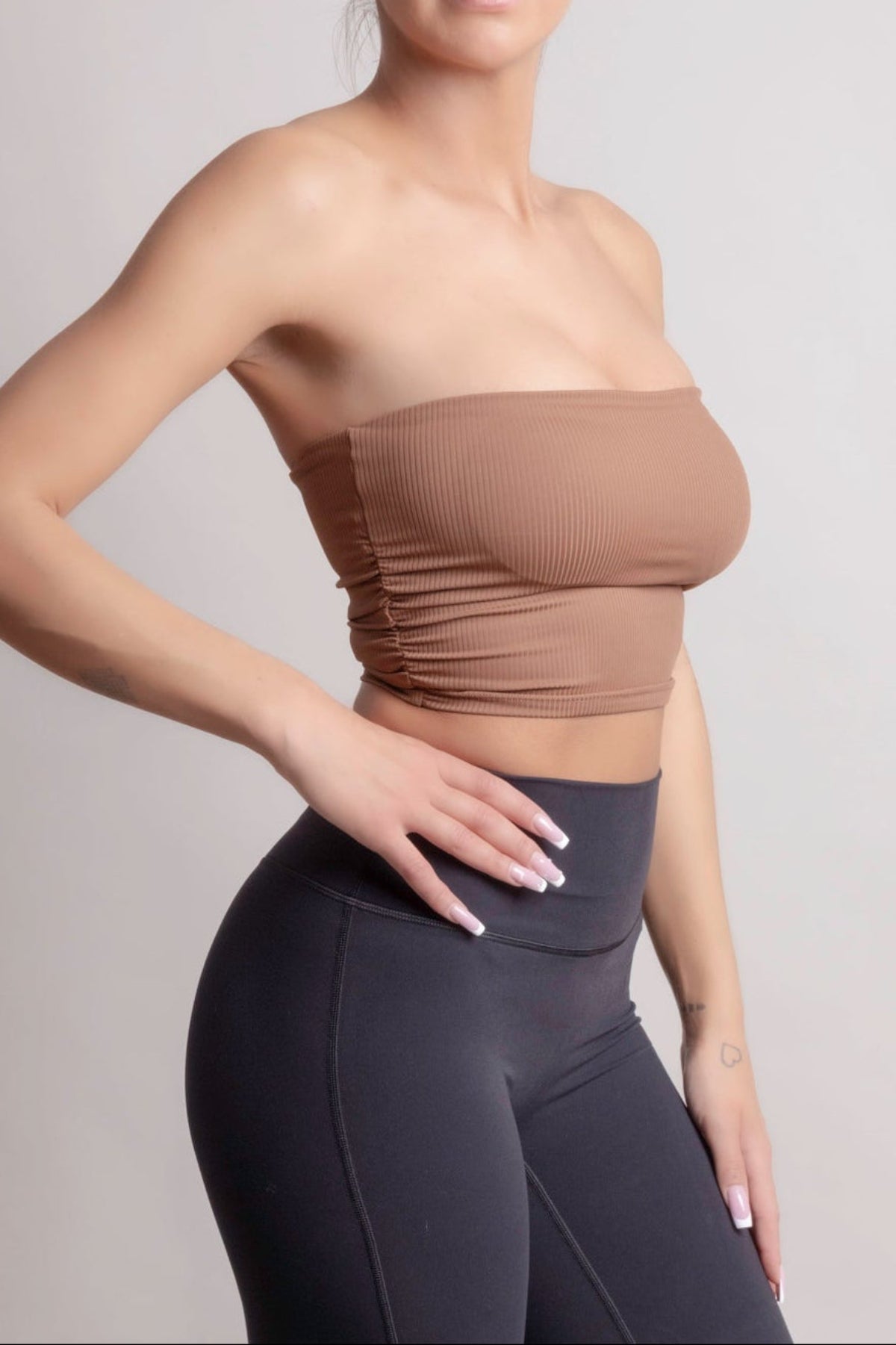 Model wearing NOIR bandeau top earth brown, featuring a seamless fit and ribbed texture, paired with high-waisted leggings.