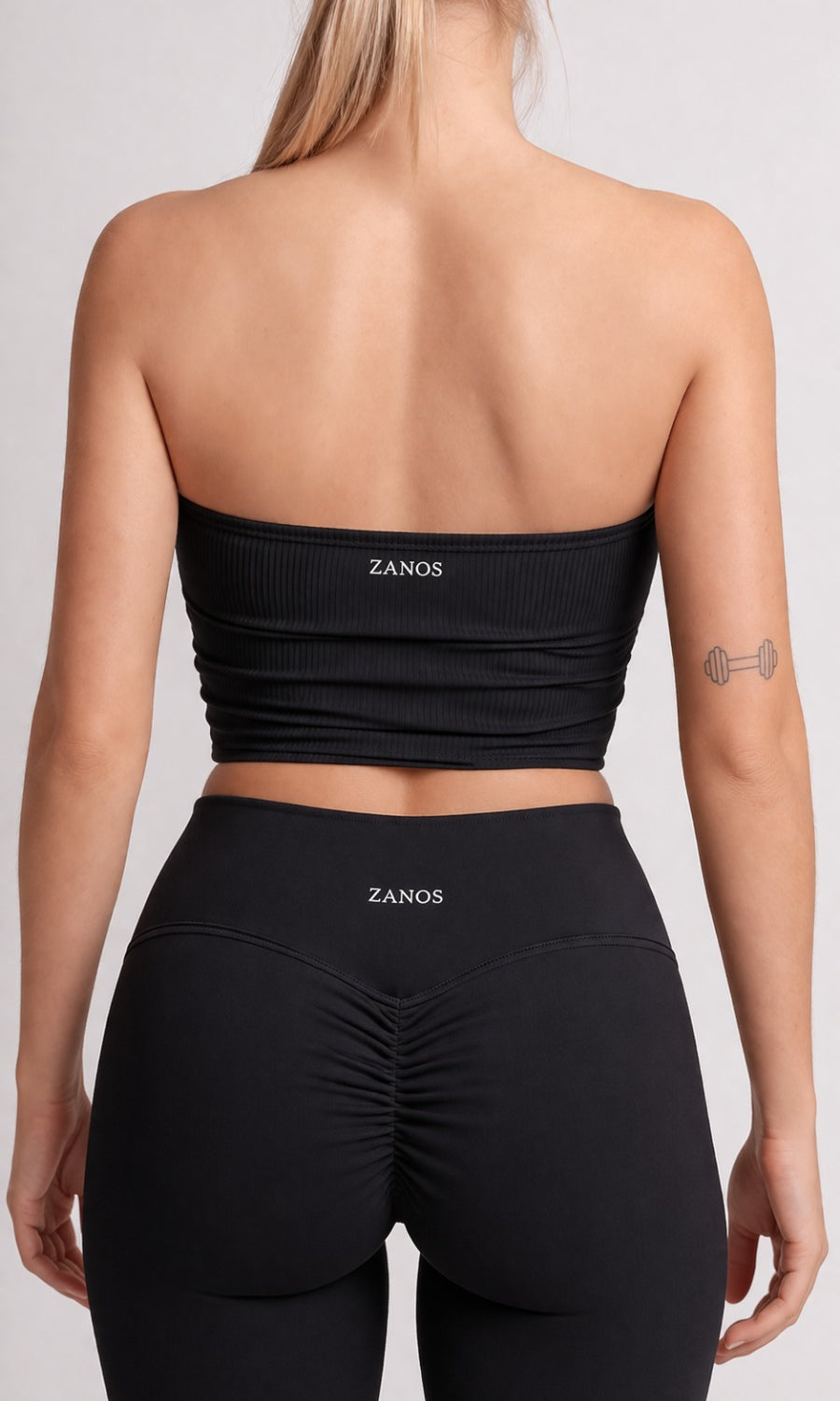 Person wearing a black strapless top and leggings with 'ZANOS' branding on a plain background