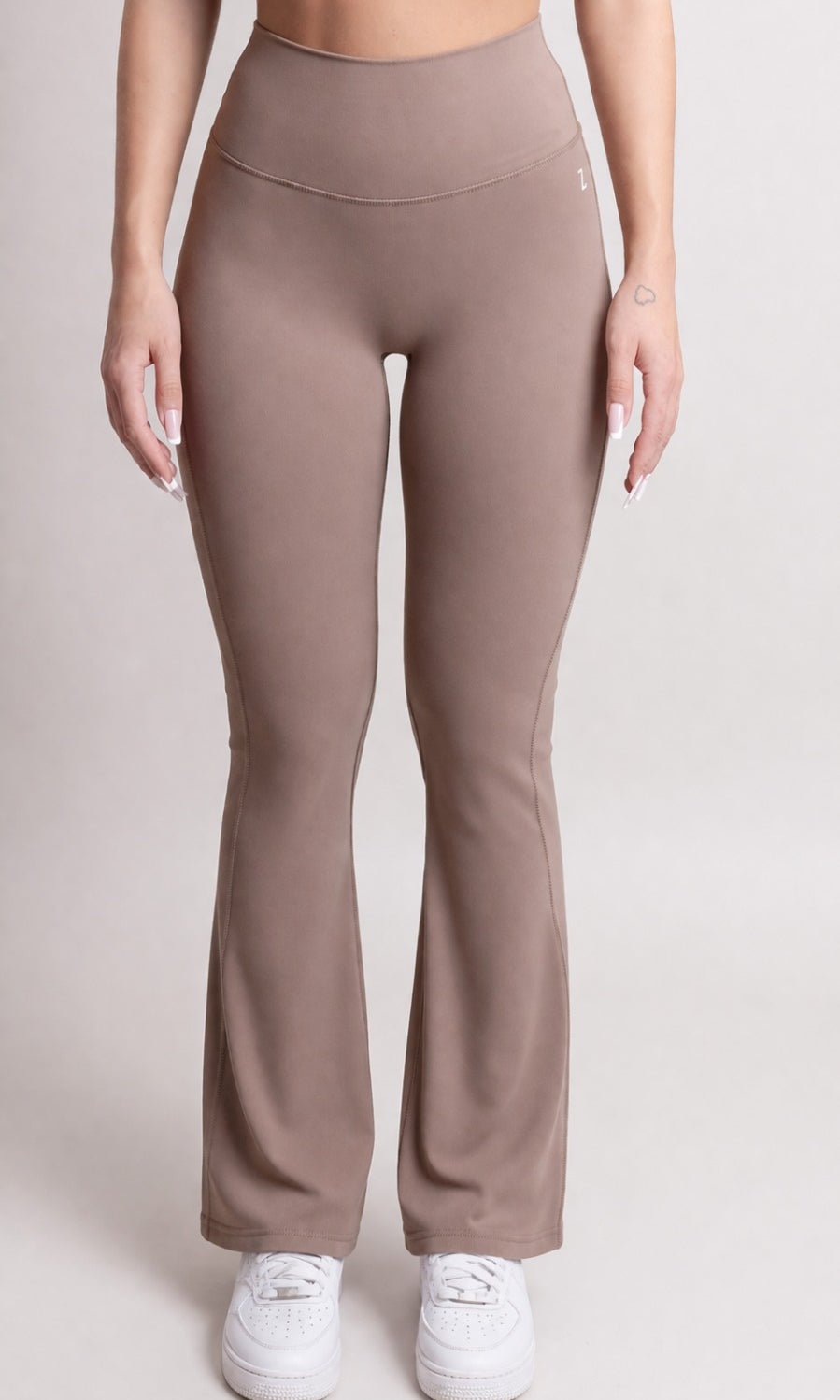 NOIR Flare Pants Brown Women model wearing high-waisted flared pants with sneakers in a neutral setting.