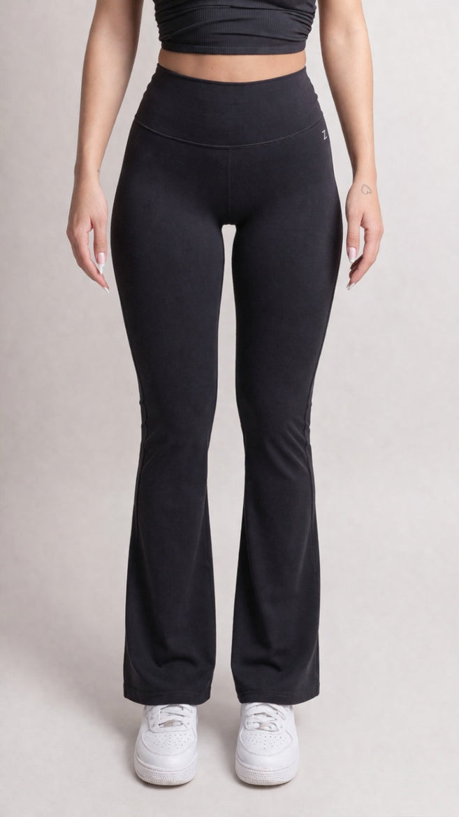 Model wearing NOIR Flare Pants Black women's high-waisted stylish flared leg pants with white sneakers.