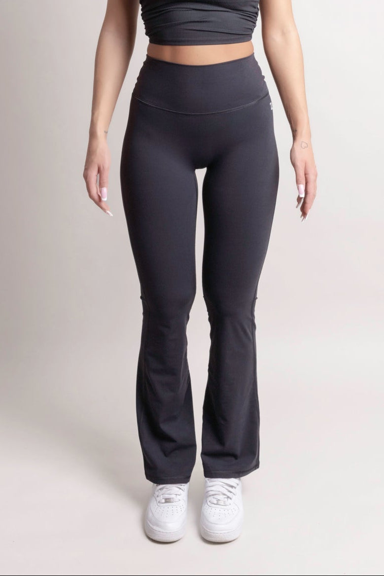 Model wearing NOIR Flare Pants Black women's high-waisted stylish flared leg pants with white sneakers.