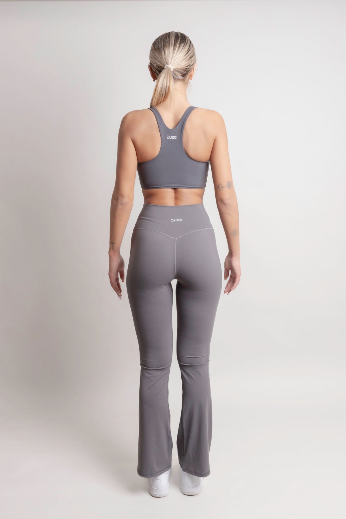 Back view of a model wearing NOIR Flare Pants Grey Women and a matching sports bra from ZANOS Apparel.