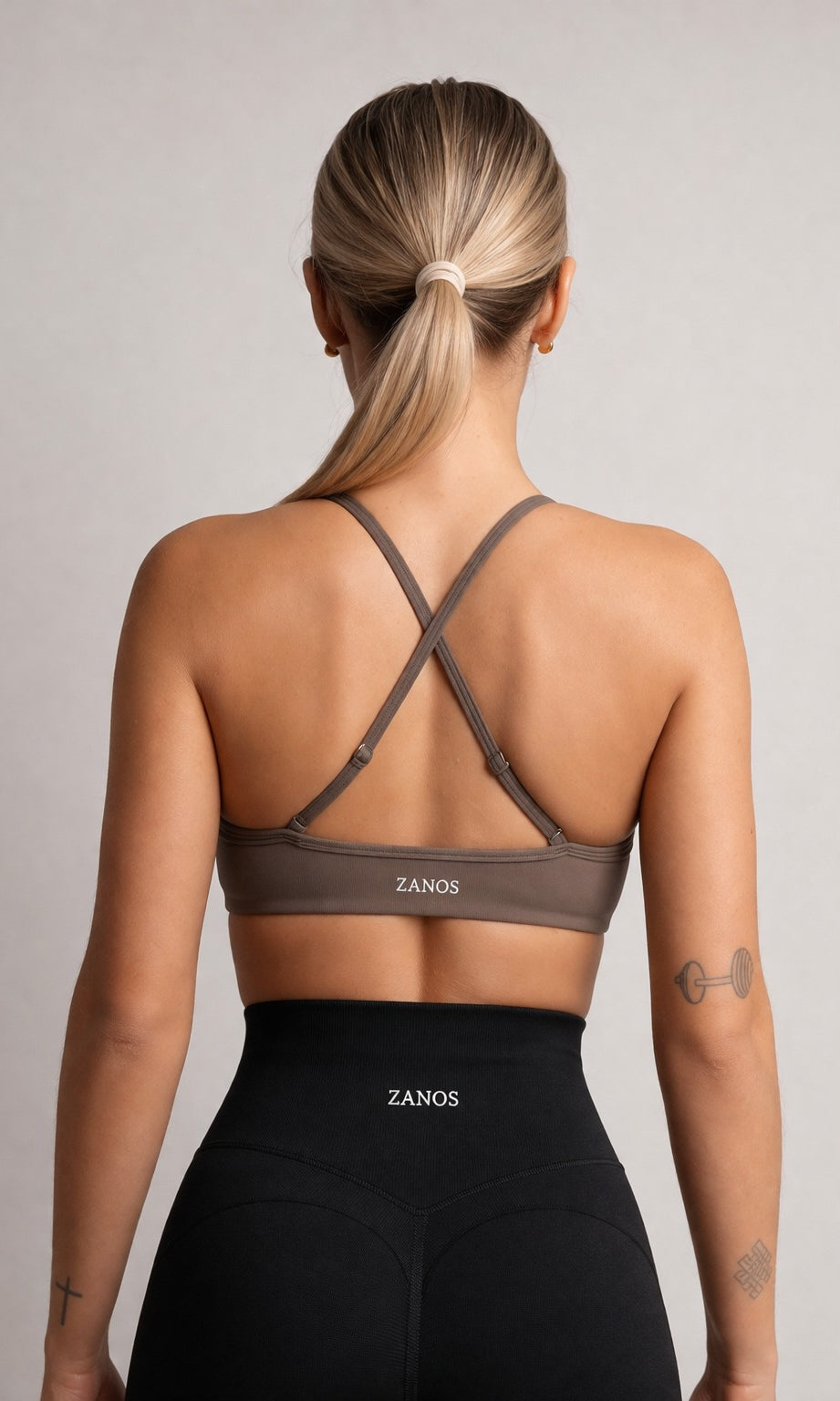 Woman wearing a brown sports bra and black leggings with 'ZANOS' branding on a plain background