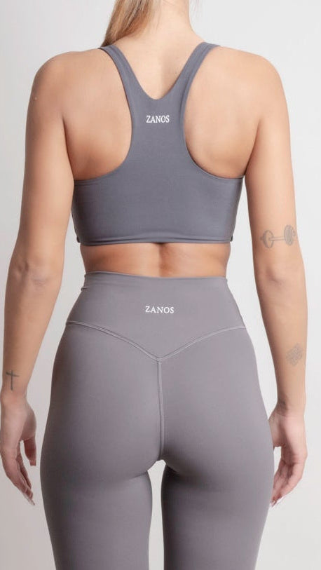 Person wearing a gray sports bra and leggings set with 'ZANOS' branding on a light gray background