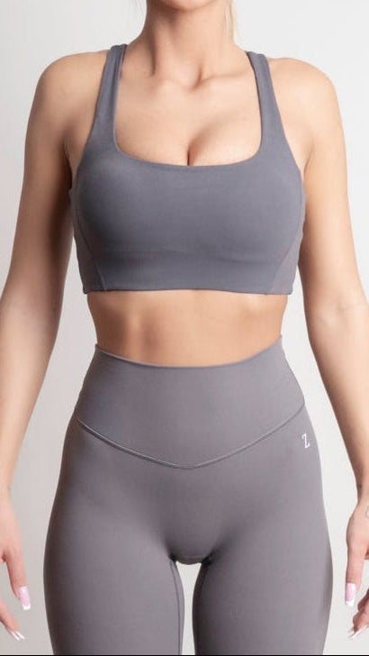 Person wearing a gray sports bra and leggings on a light gray background