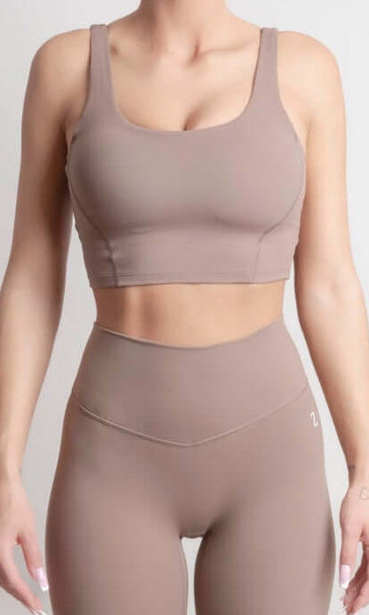 Woman wearing NOIR Sport top a beige sports bra and leggings set on a plain background