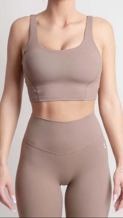 Woman wearing NOIR Sport top a beige sports bra and leggings set on a plain background
