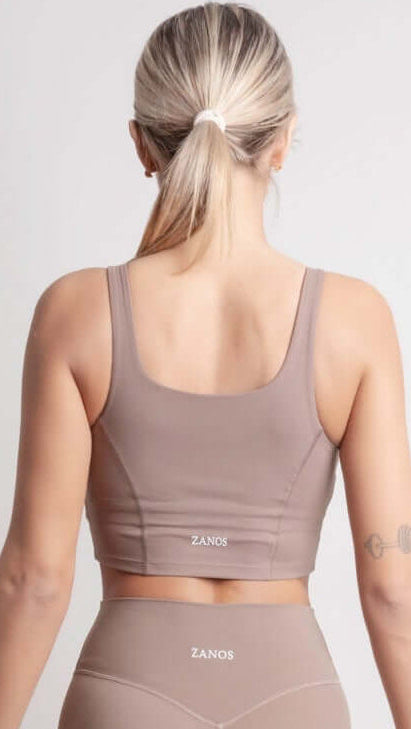 Person wearing NOIR Sport top a beige sports bra and leggings set on a white background