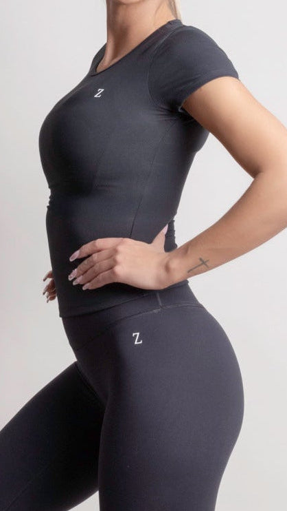 Woman wearing a NOIR t-shirt Black athletic outfit with white sneakers on a light gray background