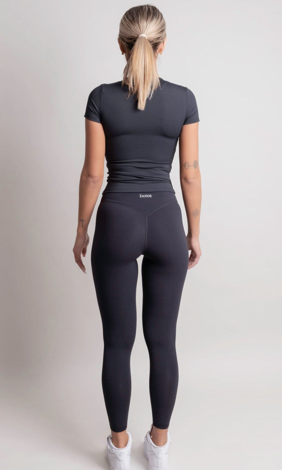 Person wearing a NOIR t-shirt black athletic outfit with 'ZANOS' branding on a light gray background