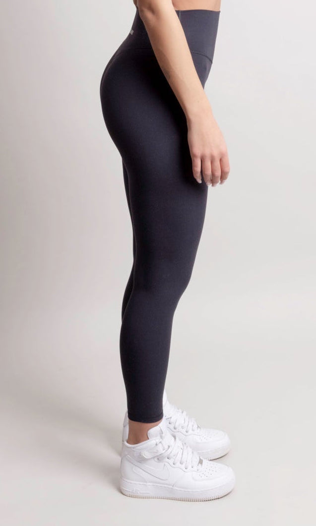 Person wearing a black athletic outfit with white sneakers on a light gray background