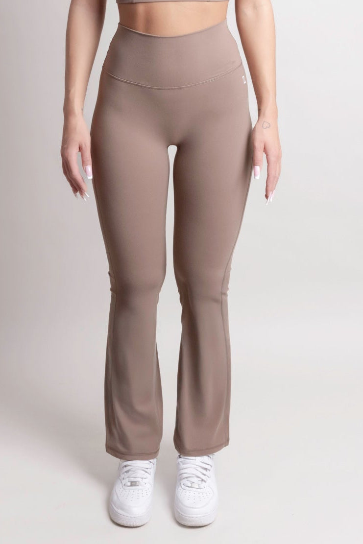 NOIR Flare Pants Brown Women model wearing high-waisted flared pants with sneakers in a neutral setting.