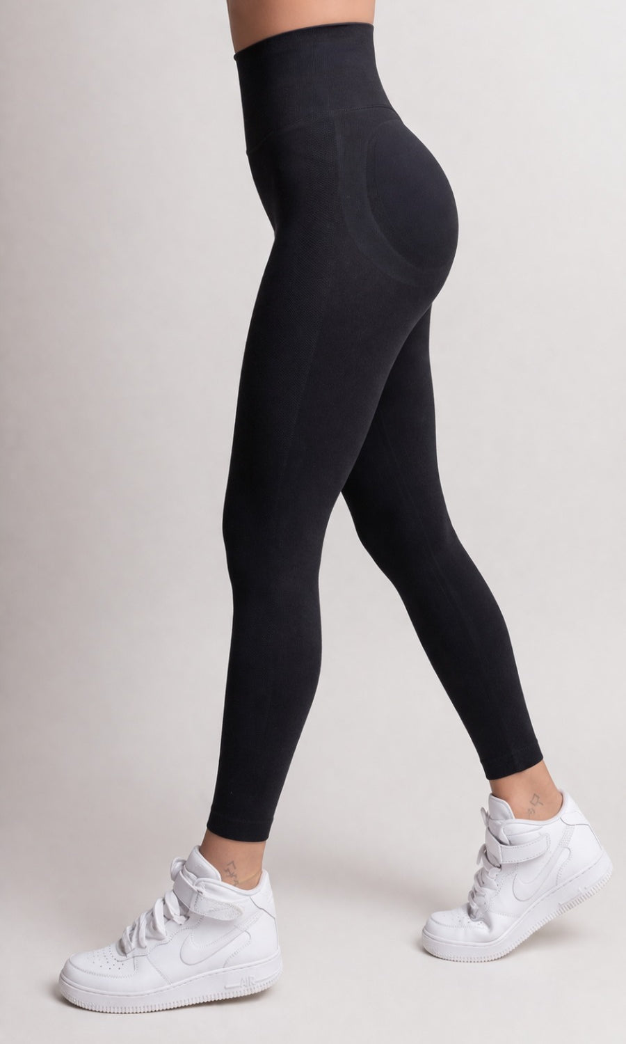 Person wearing black leggings and white sneakers on a plain background