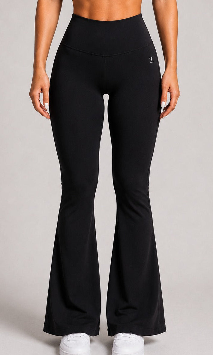 A model wearing black high-waisted flared leggings with white sneakers, shown from the waist down against a neutral gray studio background.