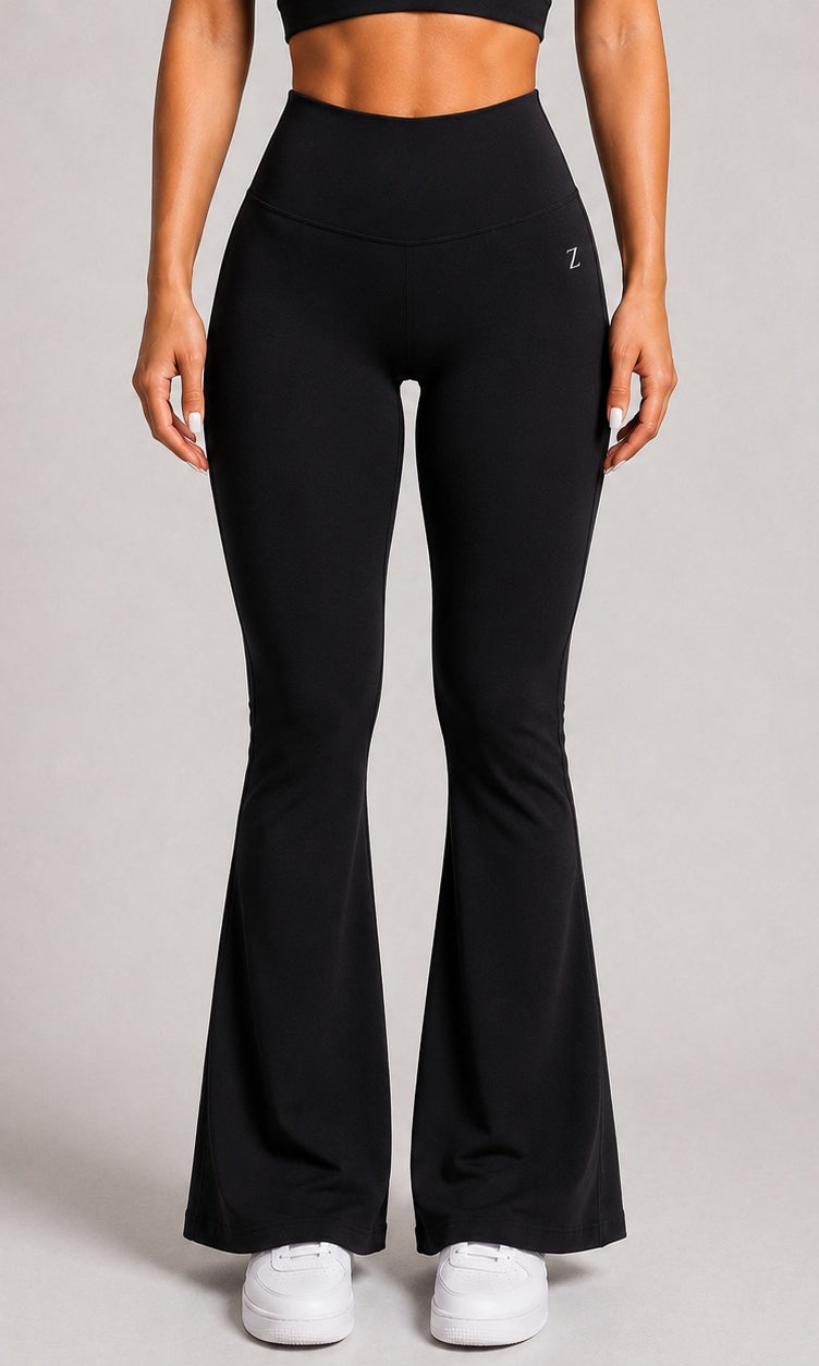 A model wearing black high-waisted flared leggings with white sneakers, shown from the waist down against a neutral gray studio background.