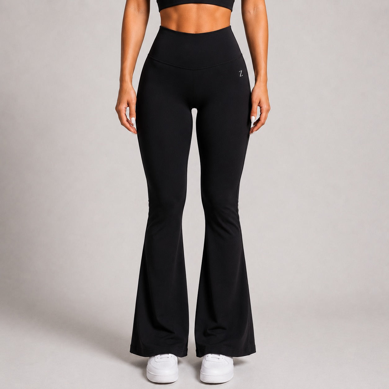 A model wearing black high-waisted flared leggings with white sneakers, shown from the waist down against a neutral gray studio background.