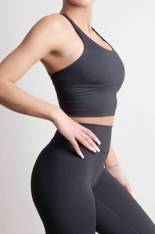 Model wearing NOIR Cross Top Black Women with leggings and sneakers, showcasing dynamic movement and comfort.