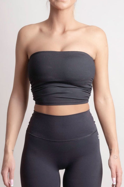 Person wearing a NOIR Bandeau Top black strapless top and leggings on a light gray background
