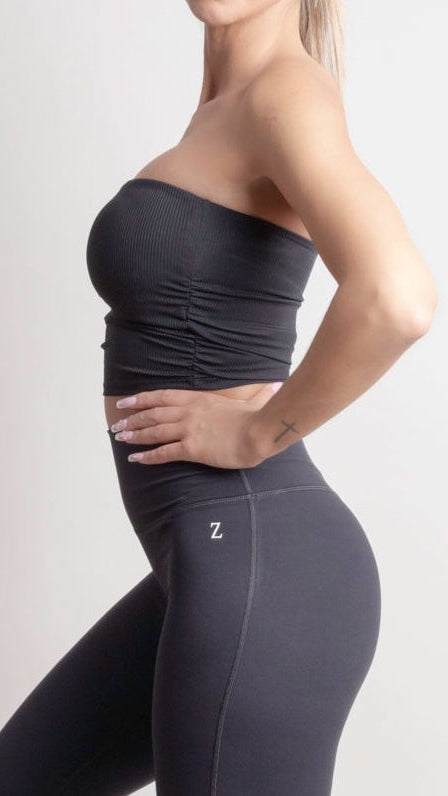 Woman wearing a NOIR Bandeau Top black strapless top and black pants on a white background