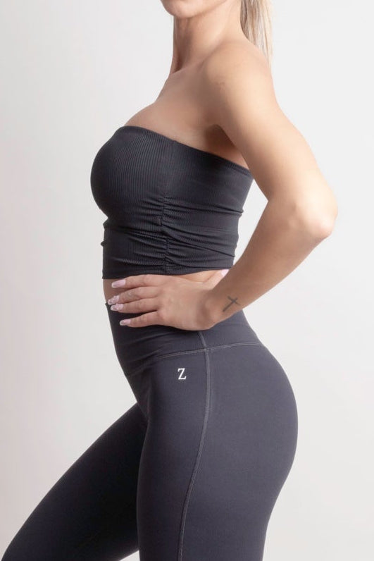 Woman wearing a NOIR Bandeau Top black strapless top and black pants on a white background