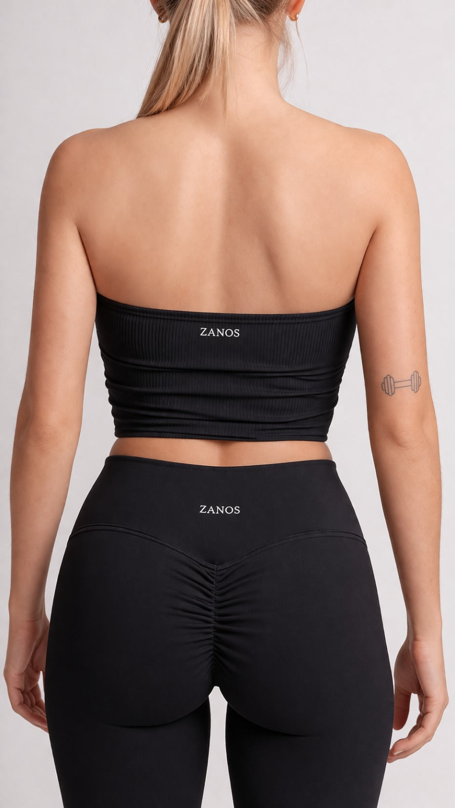 Person wearing a black strapless top and leggings with 'ZANOS' branding on a plain background