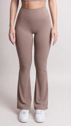 NOIR Flare Pants Brown Women model wearing high-waisted flared pants with sneakers in a neutral setting.