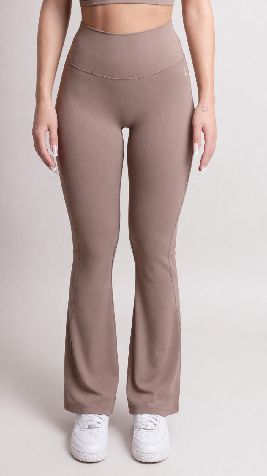 NOIR Flare Pants Brown Women model wearing high-waisted flared pants with sneakers in a neutral setting.