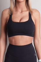 Person wearing a NOIR sculpt bra black sports bra and leggings against a neutral background