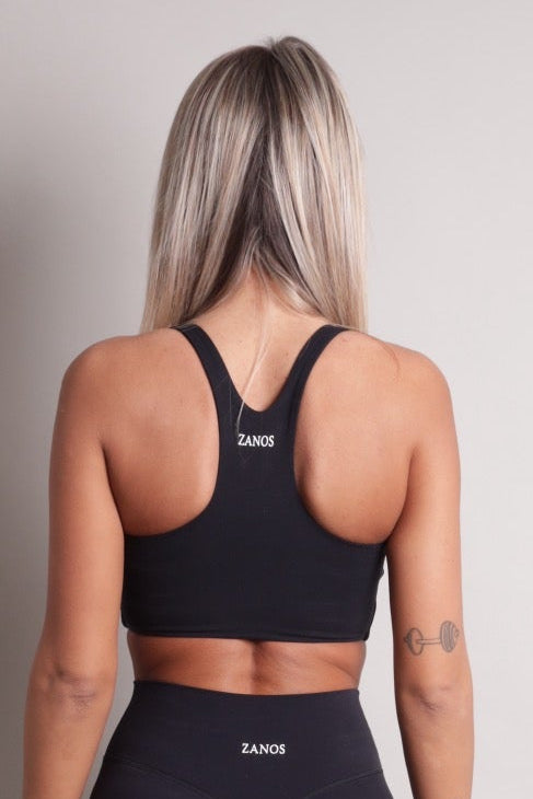Person wearing a NOIR sculpt bra black sports bra and leggings with 'ZANOS' branding on a plain background