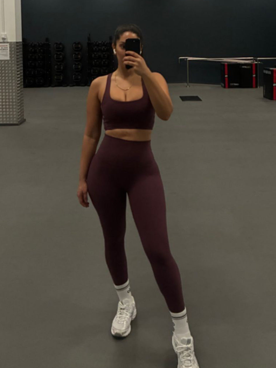 Person taking a mirror selfie wearing a maroon athletic outfit in a gym.