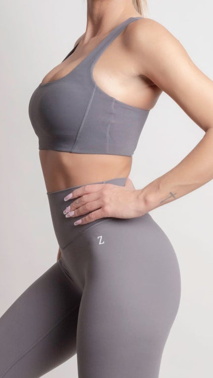 Person wearing a gray sports bra and leggings with a brand logo on a light background