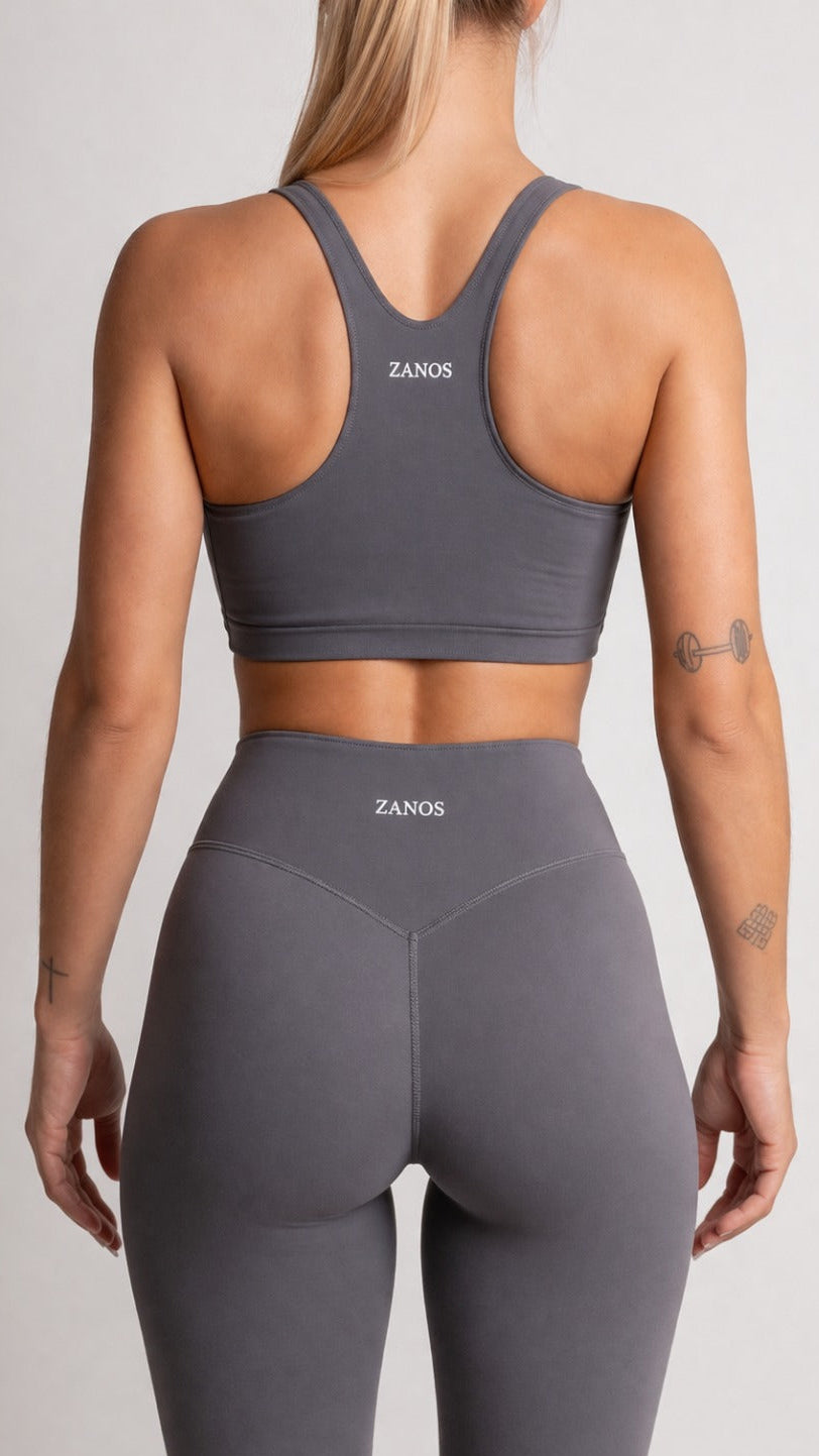 Person wearing a gray sports bra and leggings with 'ZANOS' branding on a light gray background