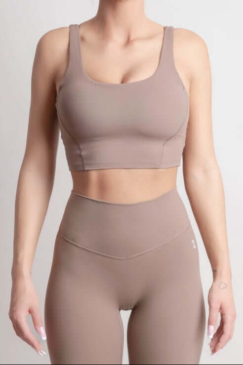 Woman wearing NOIR Sport top a beige sports bra and leggings set on a plain background