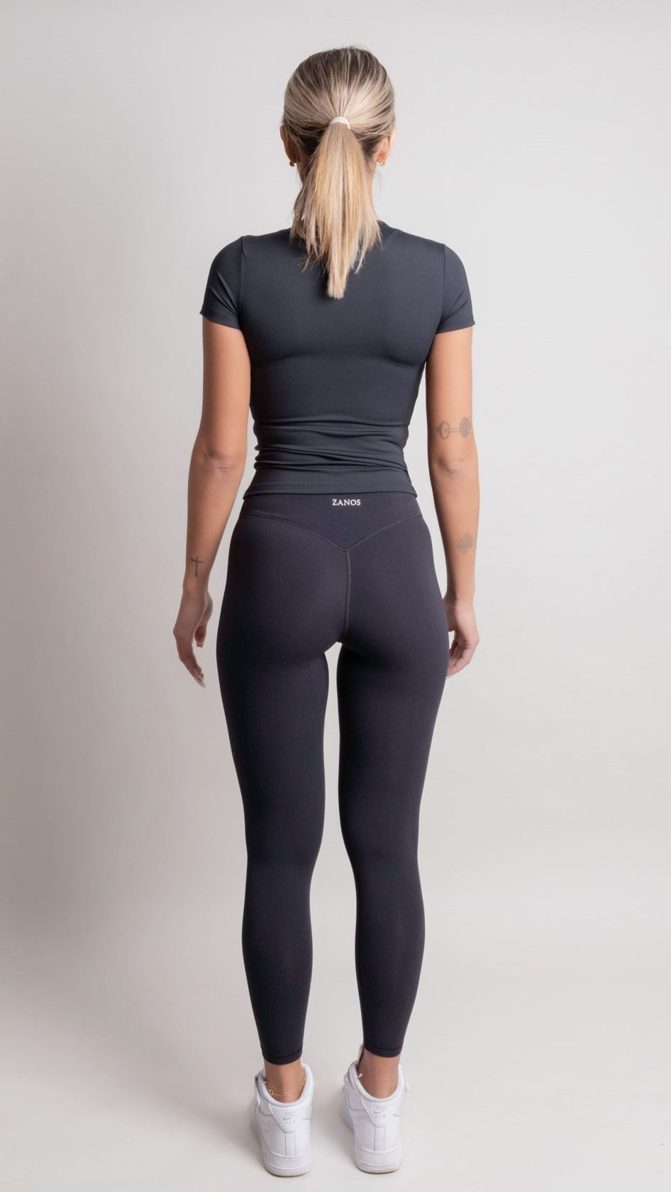 Person wearing a NOIR t-shirt black athletic outfit with 'ZANOS' branding on a light gray background