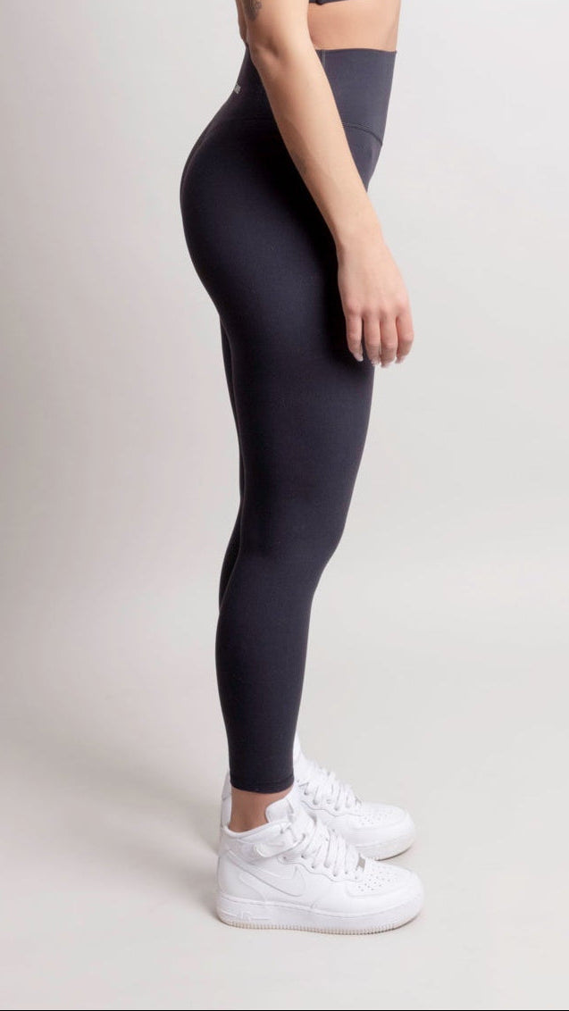 Person wearing a black athletic outfit with white sneakers on a light gray background