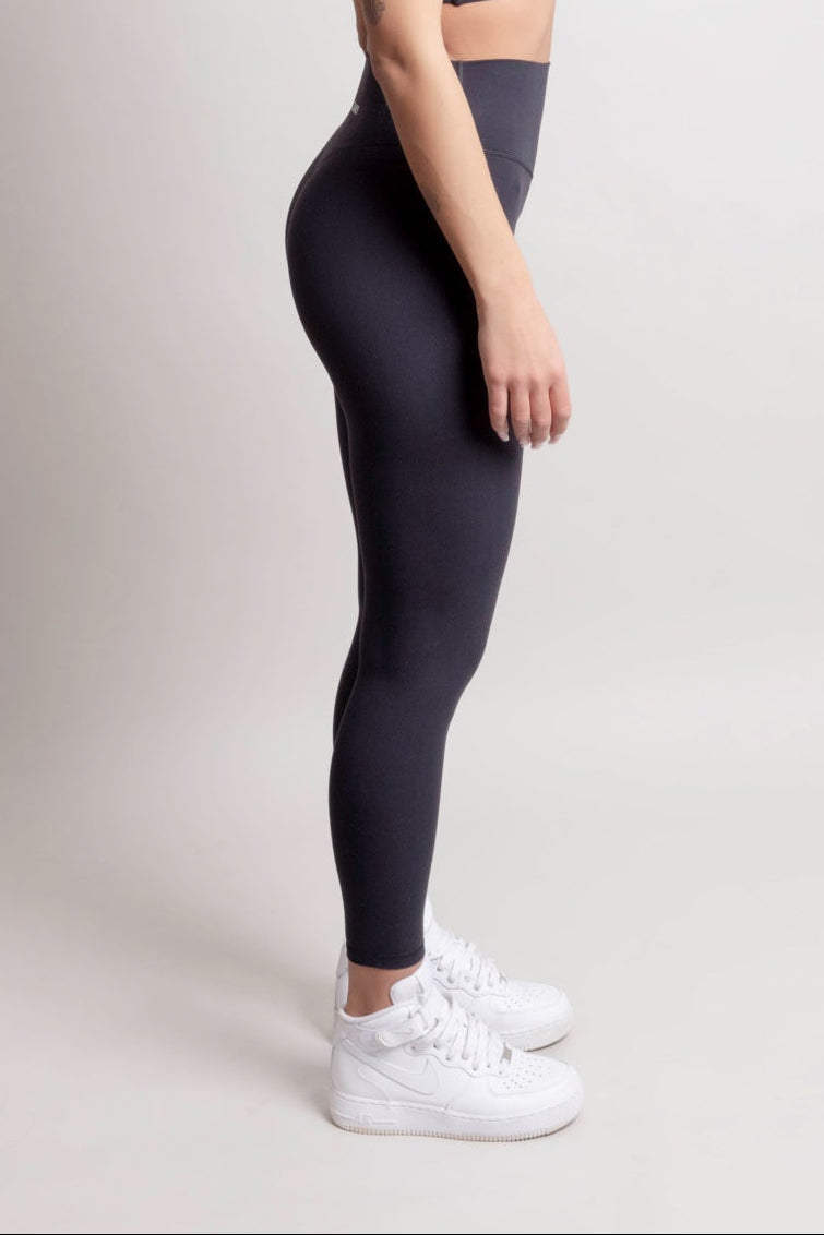 Person wearing a black athletic outfit with white sneakers on a light gray background