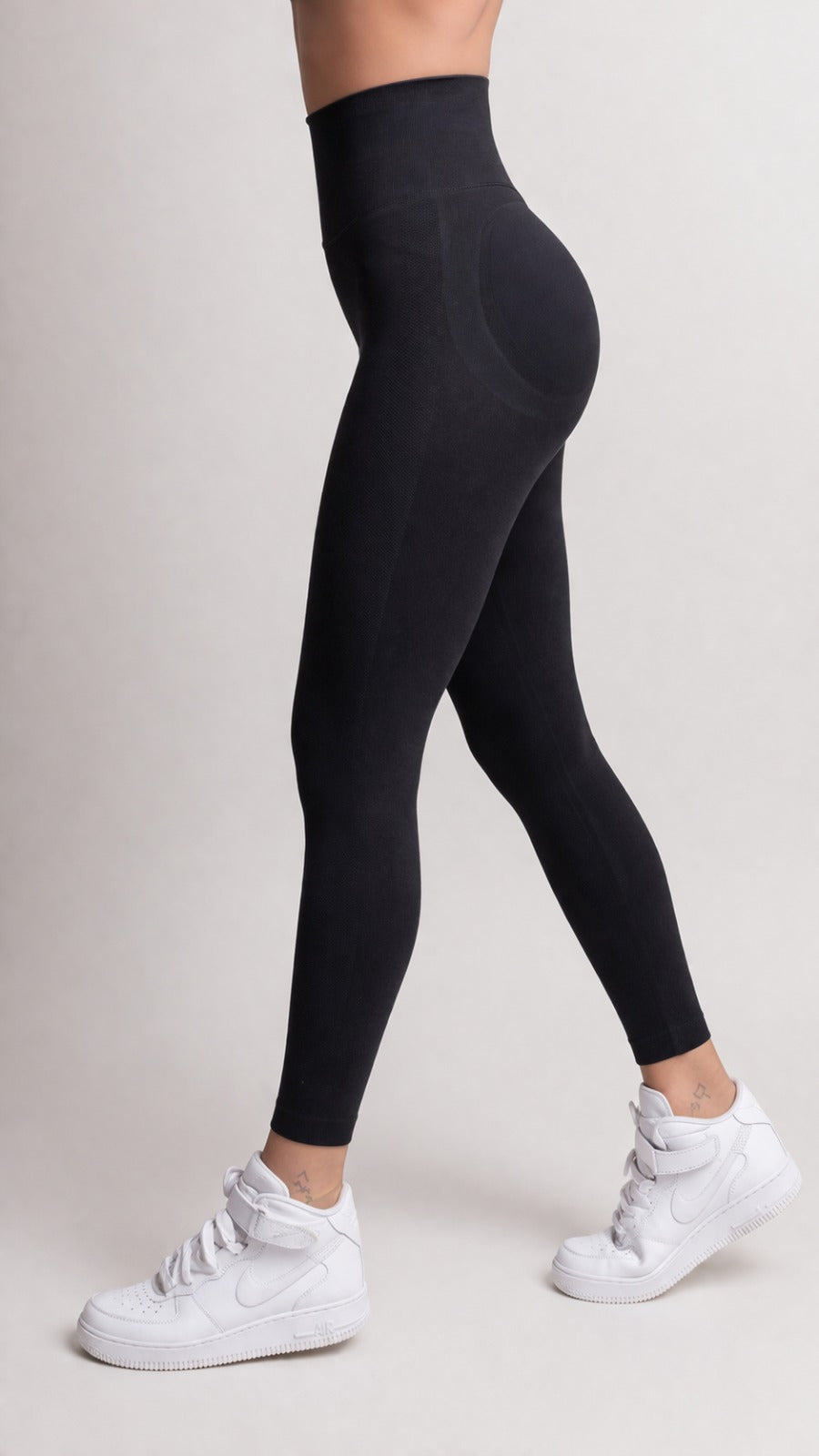 Person wearing black leggings and white sneakers on a plain background