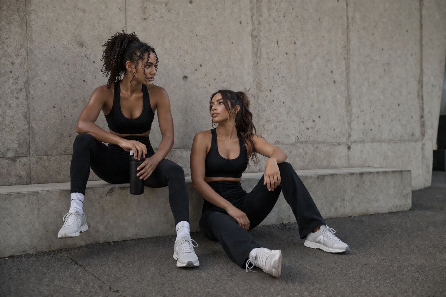Two women in athletic wear sitting on a concrete ledge.
