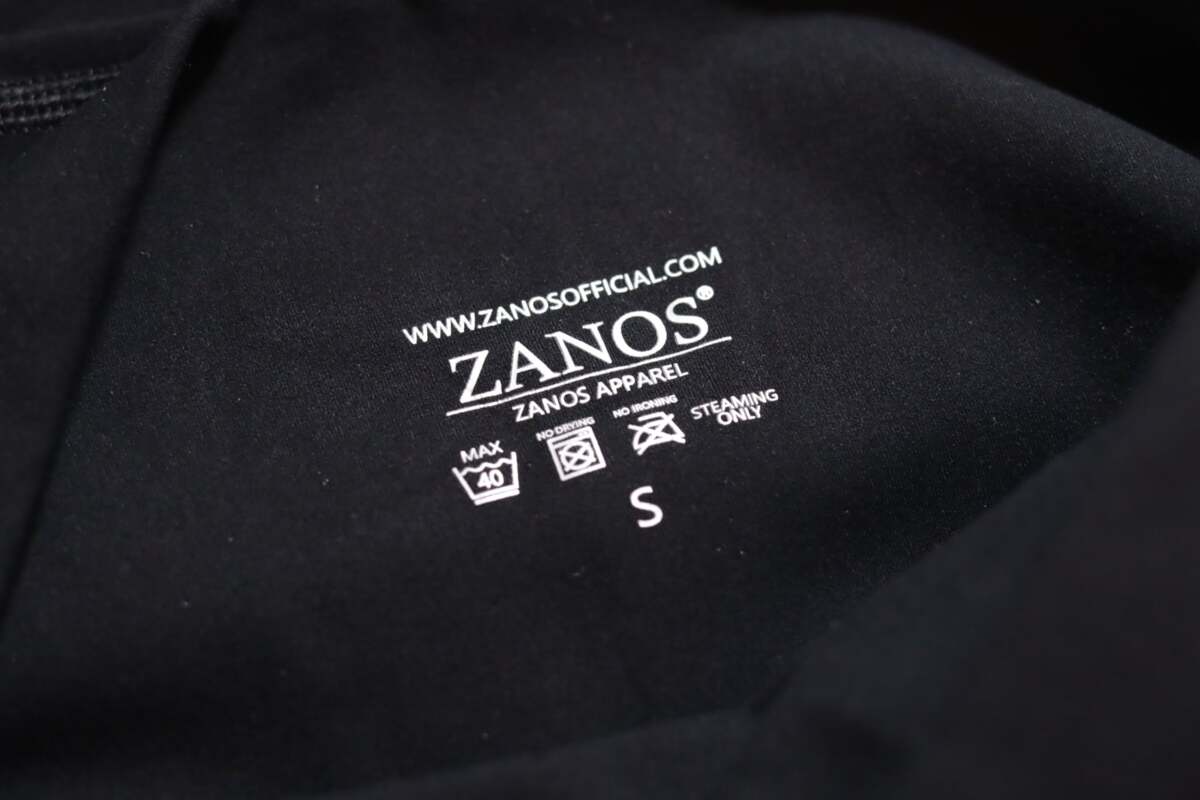 ZANOS apparel label on a black fabric background