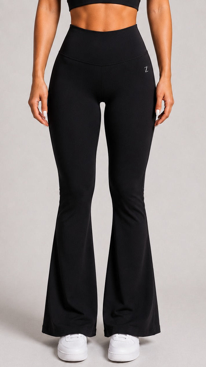 A model wearing black high-waisted flared leggings with white sneakers, shown from the waist down against a neutral gray studio background.
