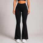 A model wearing black high-waisted flared leggings with white sneakers, shown from the waist down against a neutral gray studio background.
