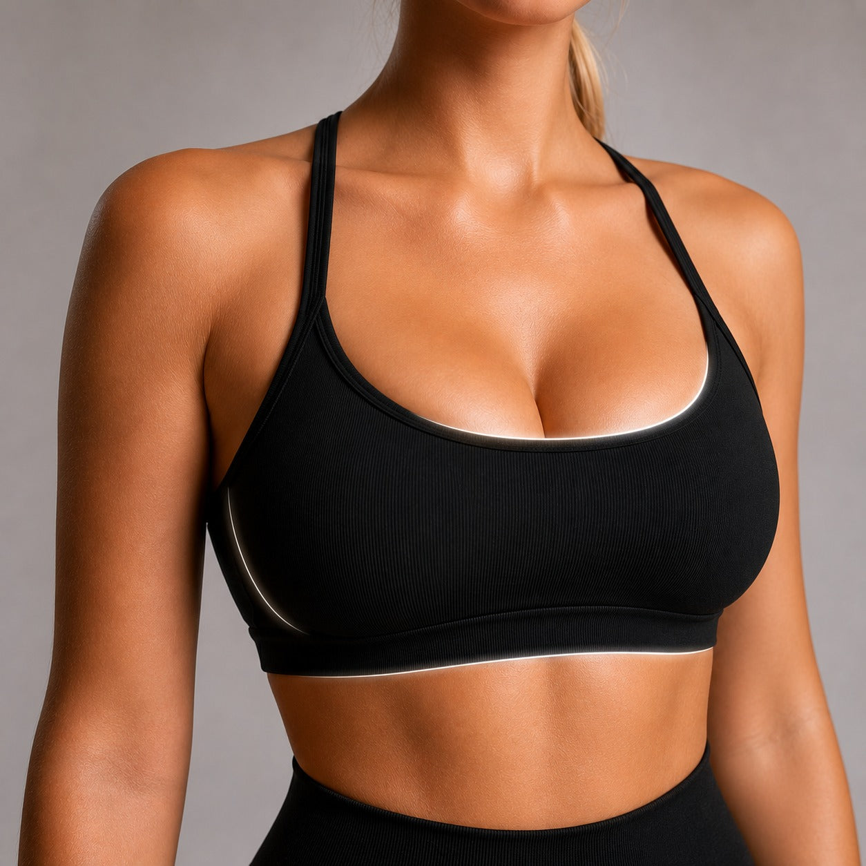 A close-up of a woman wearing a black ribbed sports bra with white piping trim along the neckline and underband, set against a neutral gray studio background.