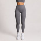 A model from the waist down wearing high-waisted, form-fitting gray leggings and white sneakers, standing against a light gray studio background.
