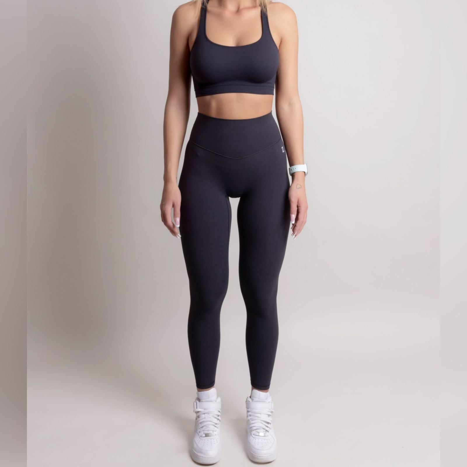 Person wearing black athletic leggings and sports bra on a plain background